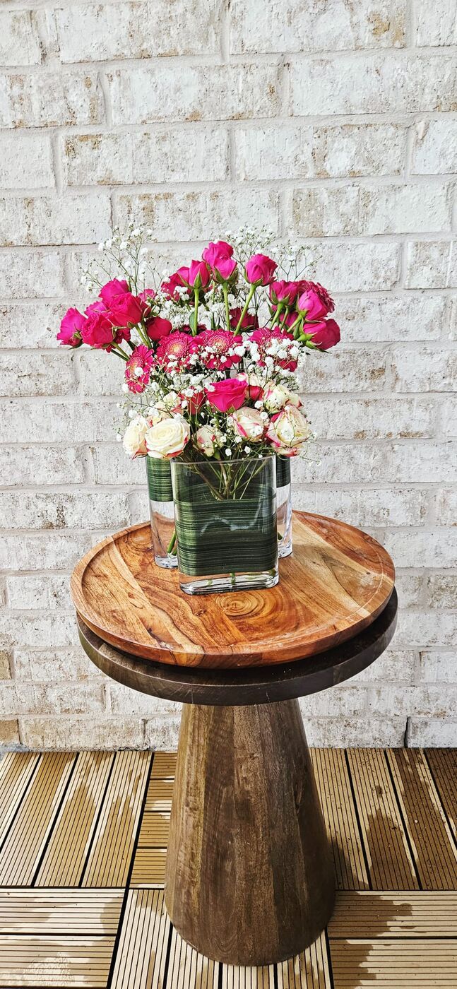 Coral garden roses with white ranunculus in a footed bowl on a wooden pedestal